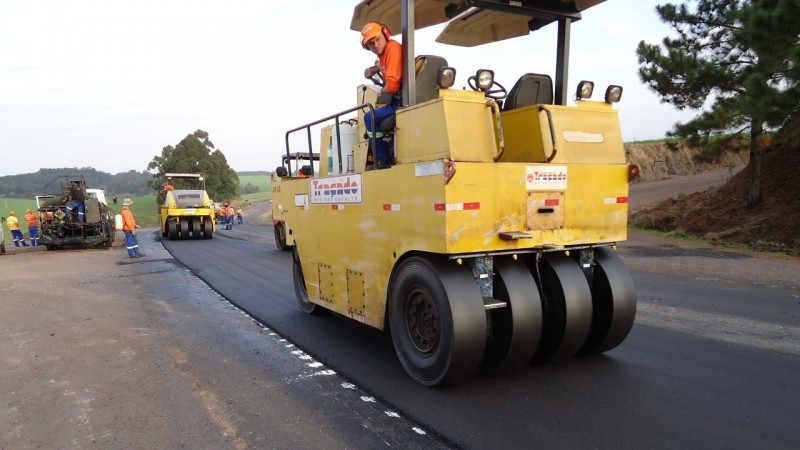 A foto mostra uma máquina de rolo compressor realizando obra de recapeamento asfáltico na rodovia ERS-324, entre Natalino e Passo Fundo. Ao fundo, outra máquina semelhante auxilia nos serviços.