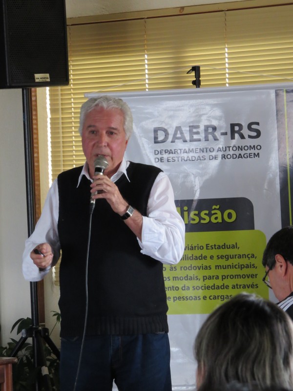 Palestrante, com banner do Daer ao fundo, fala para um público especializado.