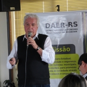 Palestrante, com banner do Daer ao fundo, fala para um público especializado.