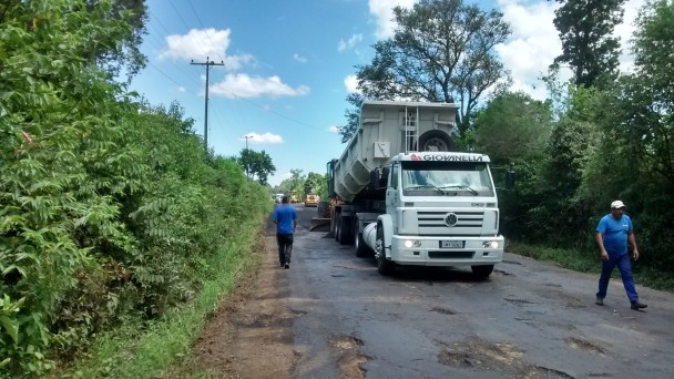 A imagem mostra uma pista com buracos. Nela, está um caminhão e dois homens que serão responsáveis pela restauração da pista.
