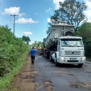 A imagem mostra uma pista com buracos. Nela, está um caminhão e dois homens que serão responsáveis pela restauração da pista.